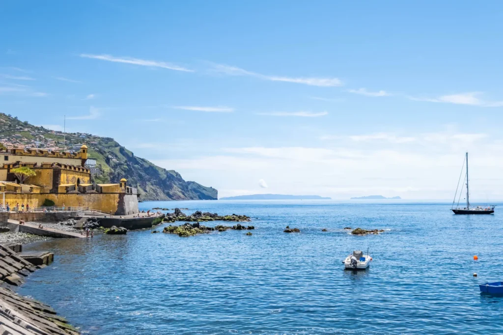 Seaside view with yellow fort, sailboats, and distant islands.