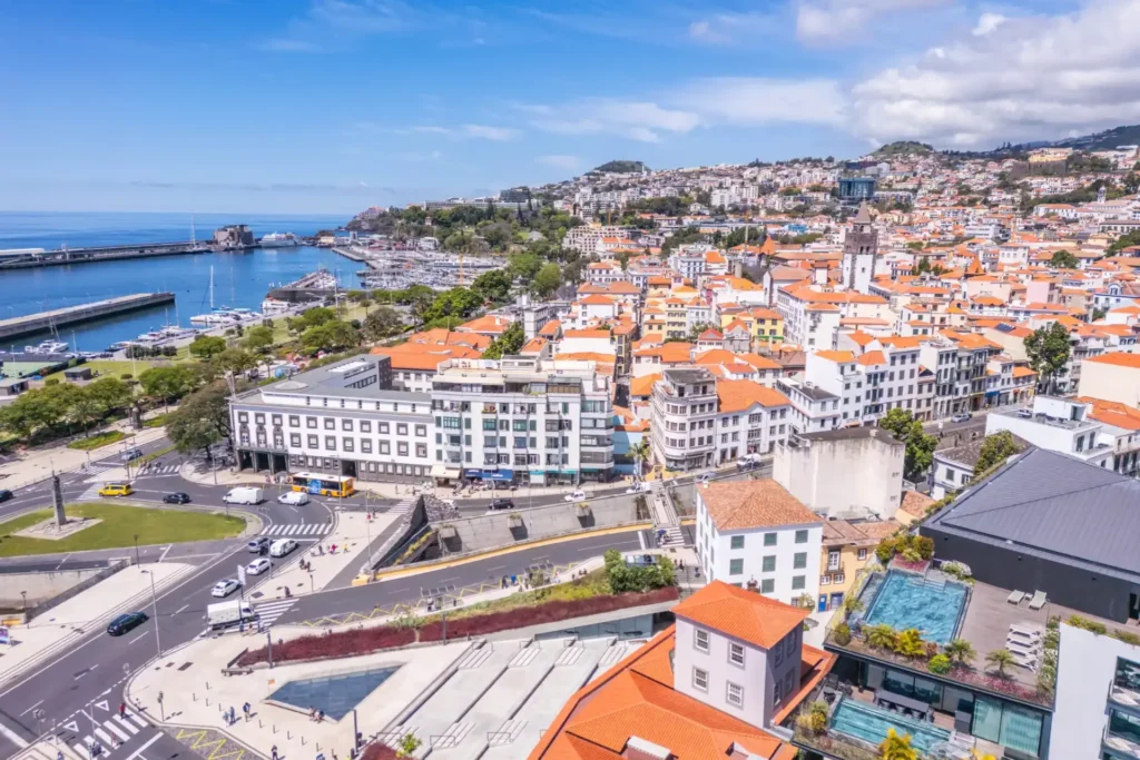 Bustling coastal cityscape with red rooftops, marina, and surrounding hills.